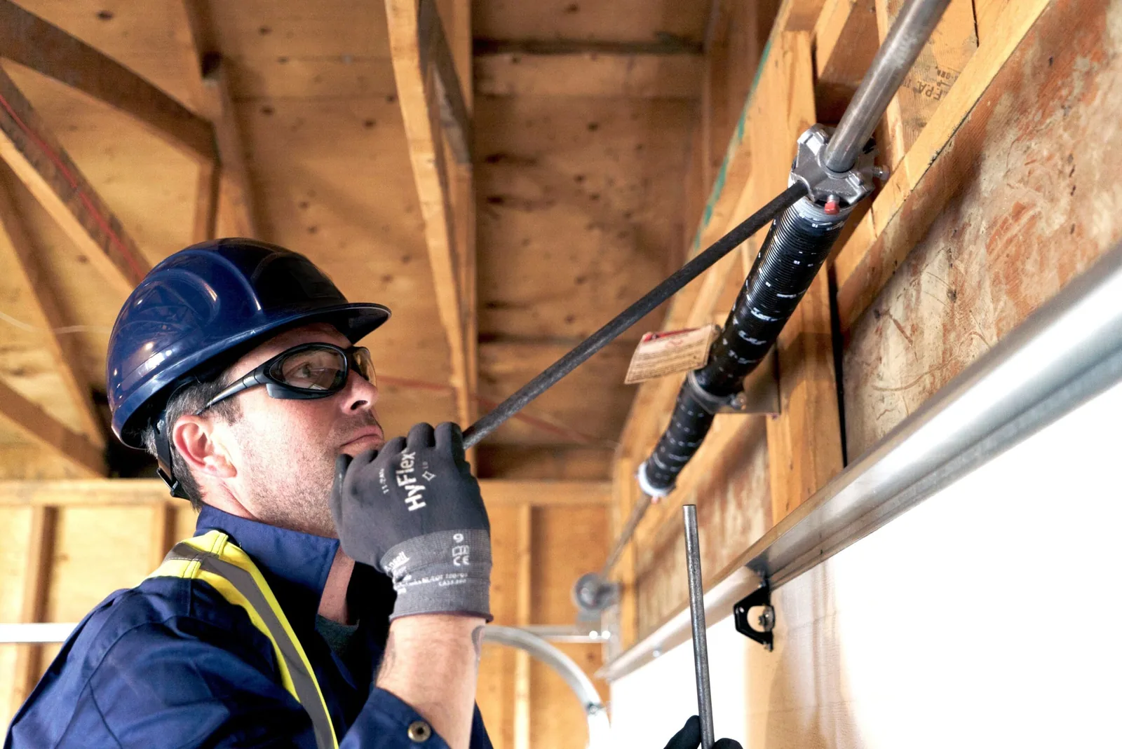 A&E technician winding a garage door torsion spring with winding bars